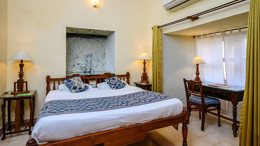 A bedroom with a bed, a desk, an air conditioner, and two small windows at Tijara Fort-Palace - 19th Century, Alwar.
